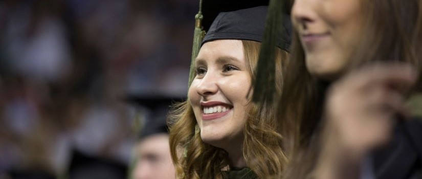 特写一名女性的脸，她戴着毕业帽，微笑着坐在UofSC毕业典礼上。