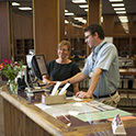 一名图书管理员在托马斯·库珀图书馆的参考服务台帮助一位顾客。两个人都站在柜台前，看着电脑显示器。