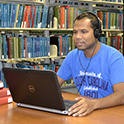 学生坐在图书馆书架前，戴着耳机听笔记本电脑里的音乐
