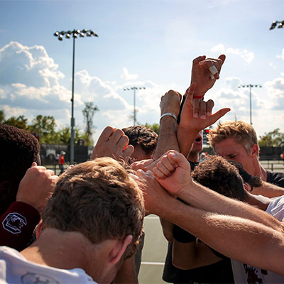 网球场上的学生们抱在一起，举起手臂。