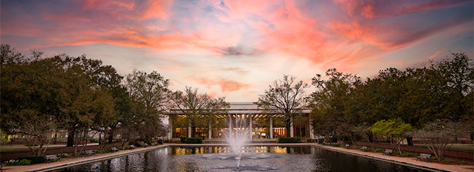 托马斯·库伯图书馆坐落在倒影池的喷泉后面，在令人惊叹的紫色和红色的夕阳前。