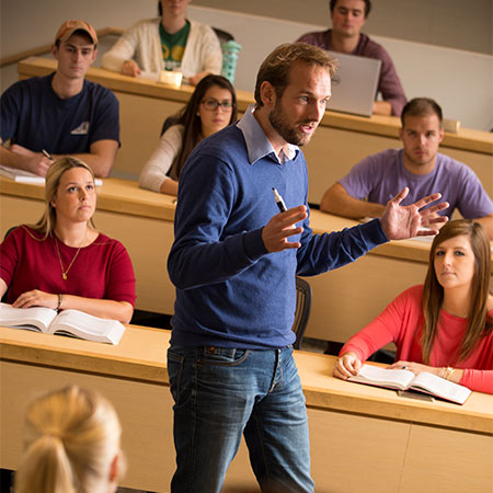 教授在教室里讲课，学生们坐在一排排的桌子上。