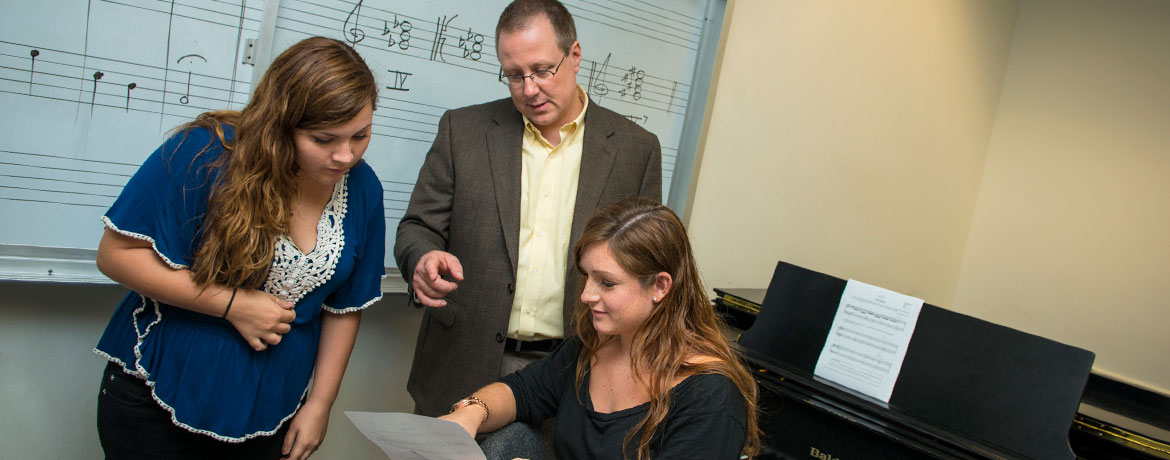 两个学音乐的学生在一间有钢琴和白板的练习室里向教授咨询
