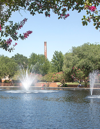 喷泉在反射池中，周围是砖路和长凳，背景是南加州大学的大烟囱。
