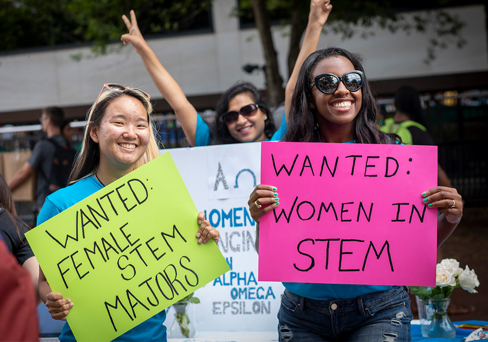 学生们在学生组织博览会上举着牌子，上面写着“招聘STEM专业的女性”。