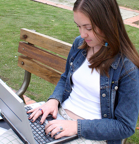 一名穿着牛仔夹克的白人妇女在公共长椅上用笔记本电脑工作