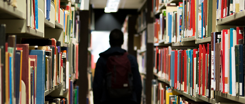一个学生走在图书馆的两个书架之间。
