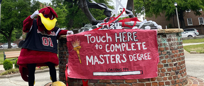 UofSc吉祥物自大指向一个标志说触摸这里完成硕士学位的火炬手雕像的底部。