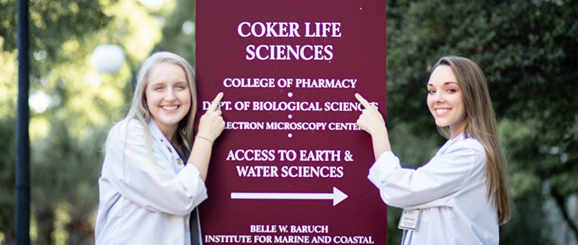 两个学生指着科克生命科学大楼的标志