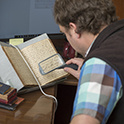 一个人使用手持放大镜阅读手稿中的手写文本的俯视图。书放在桌子上的书架上。