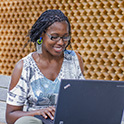 一个面带微笑、坐在笔记本电脑前工作的人。略微倾斜的正面视图显示的是笔记本电脑的顶部，而不是屏幕。