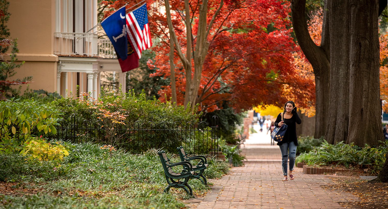 学生走在一条砖砌的小路上，有长凳和总统的房子，国旗、美国国旗和大学国旗飘扬。