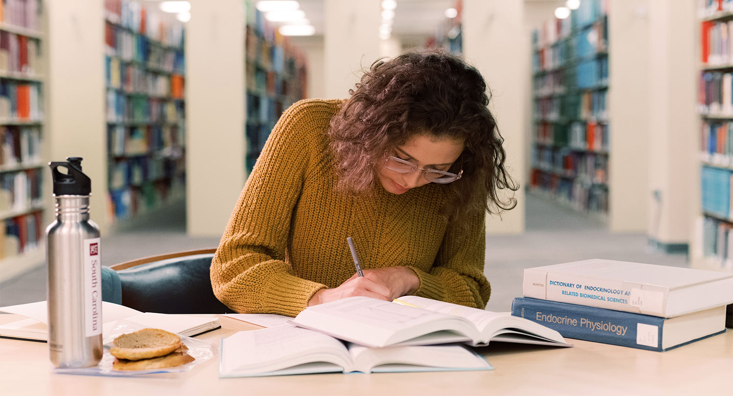 一个学生俯身在图书馆的一张桌子上学习。