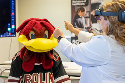 在临床场景中，一个穿着实验室大褂、戴着虚拟现实眼镜的人在科奇面前举起双手。
