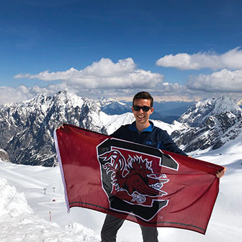 一名学生举着gameccock旗帜站在白雪覆盖的山顶上。