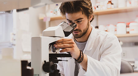 一个穿着实验服的学生正在看显微镜。