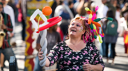 在露天市场上，一个人脸上涂着颜料，手里拿着气球动物。