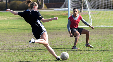 两名学生在男女同校的足球队踢球，前景的球员在踢球，另一个在防守球门。