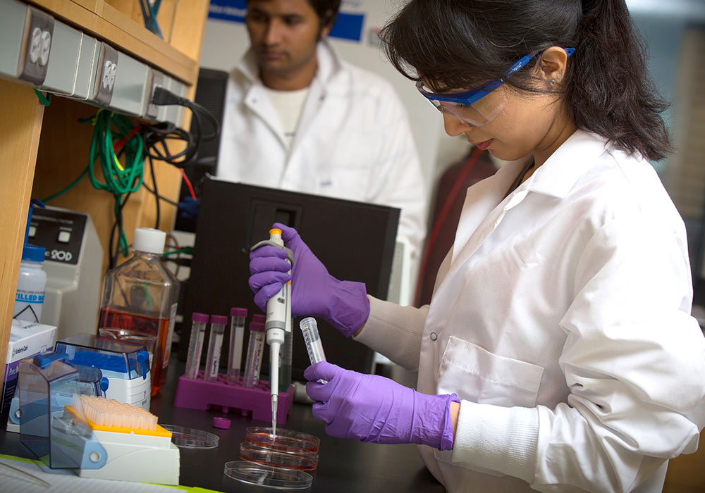 研究生穿着实验服，戴着护目镜和手套，在试管中移液。