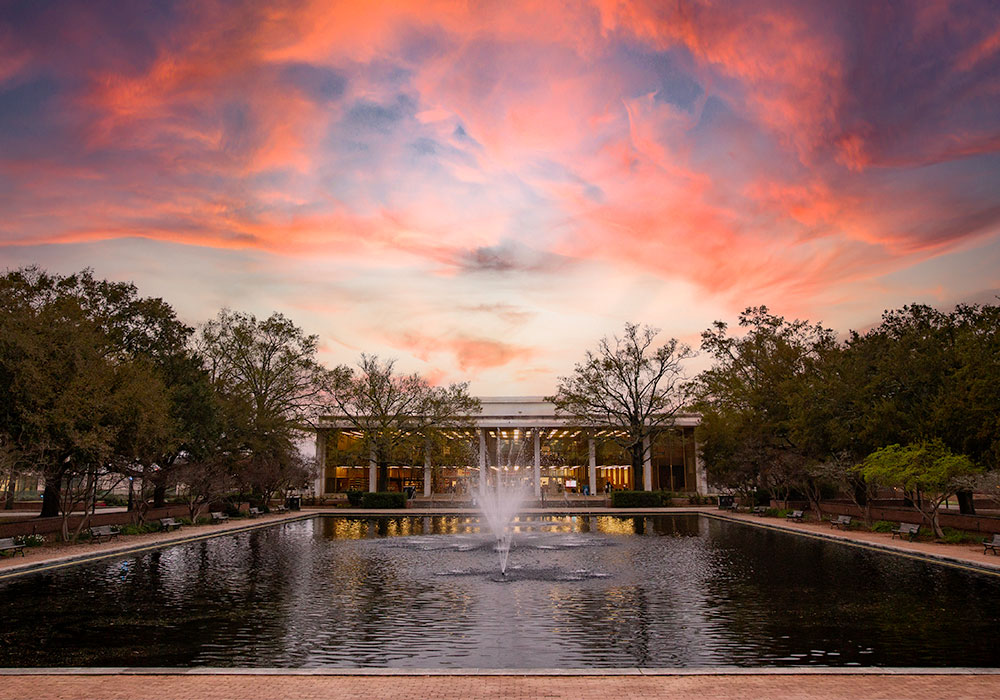 托马斯·库珀图书馆坐落在反射池的喷泉后面，在令人惊叹的紫色和红色日落前。