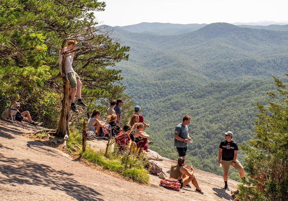 一群学生在山坡上闲逛，俯瞰远处群山环绕的山谷美景。