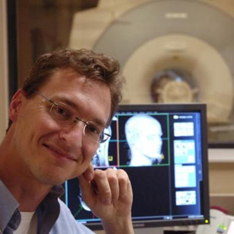克里斯·罗登(Chris Rorden)坐在电脑前看大脑图像。背景是一台核磁共振成像仪。