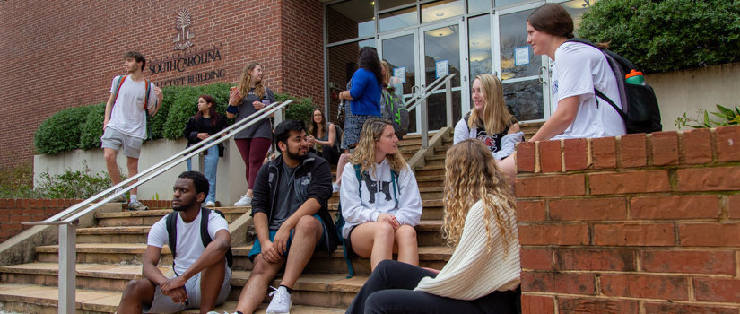 一群不同的学生坐在外面一座砖砌建筑前的台阶上。他们被分成不同的小组，互相交谈。