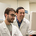 Michael Gower博士在实验室里斜靠在研究生的肩膀上。