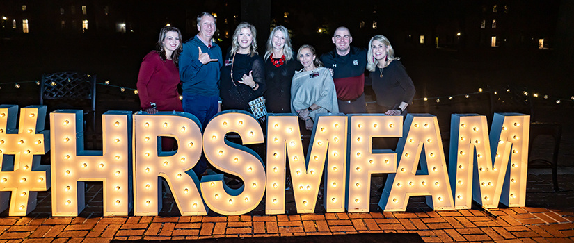 七名参加2022年HRSM返校派对的人在拼写#HRSMFAM的大字母后面合影。