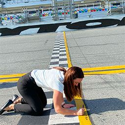 茱莉亚·麦卡利尔跪在代托纳赛道上，在那个传奇赛道的人行道上签下了她的名字
