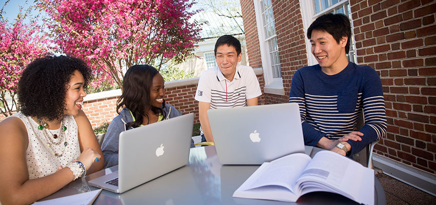 四名学生坐在SJMC露台的一张桌子旁，手里拿着笔记本电脑