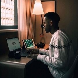 在光线昏暗的房间里，一名UofSC学生坐在书桌前。他右手边有一台iPad，他的笔记本电脑在谷歌主页上打开
