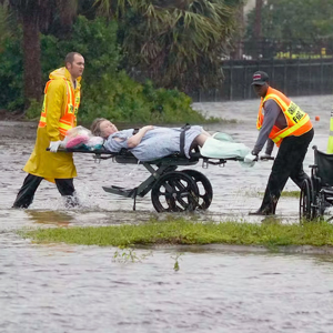 在佛罗里达州，两名医护人员用担架抬着一名妇女穿过洪水