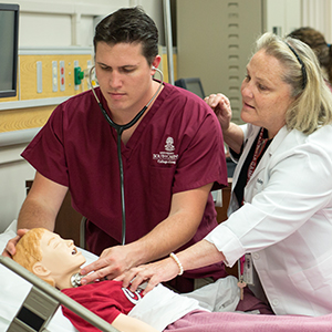一名护理系学生在人体模型上练习，而教授在一旁观察。