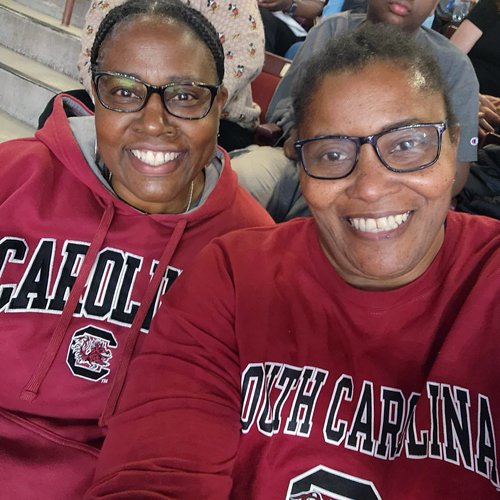 两个女人佩戴石榴石南卡罗来纳州运动衫坐在看台上看一场球赛