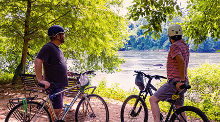 两个骑着自行车的人停在一条俯瞰河流的林间小路上。