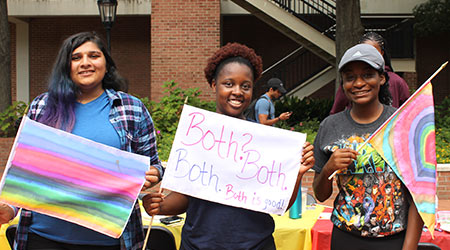 三个学生微笑着拿着他们制作的LGBTQ+旗帜。
