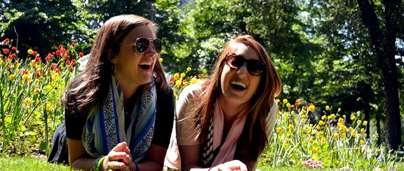 两个女学生躺在草地上在床前的花在一个晴朗的日子,笑着,戴着墨镜
