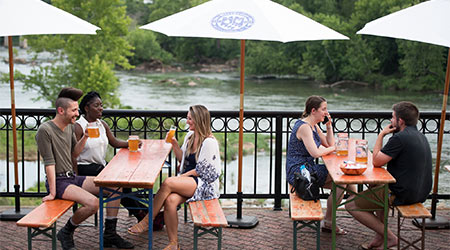 人们坐在户外的桌子旁，打着雨伞，眺望着河上的风景。