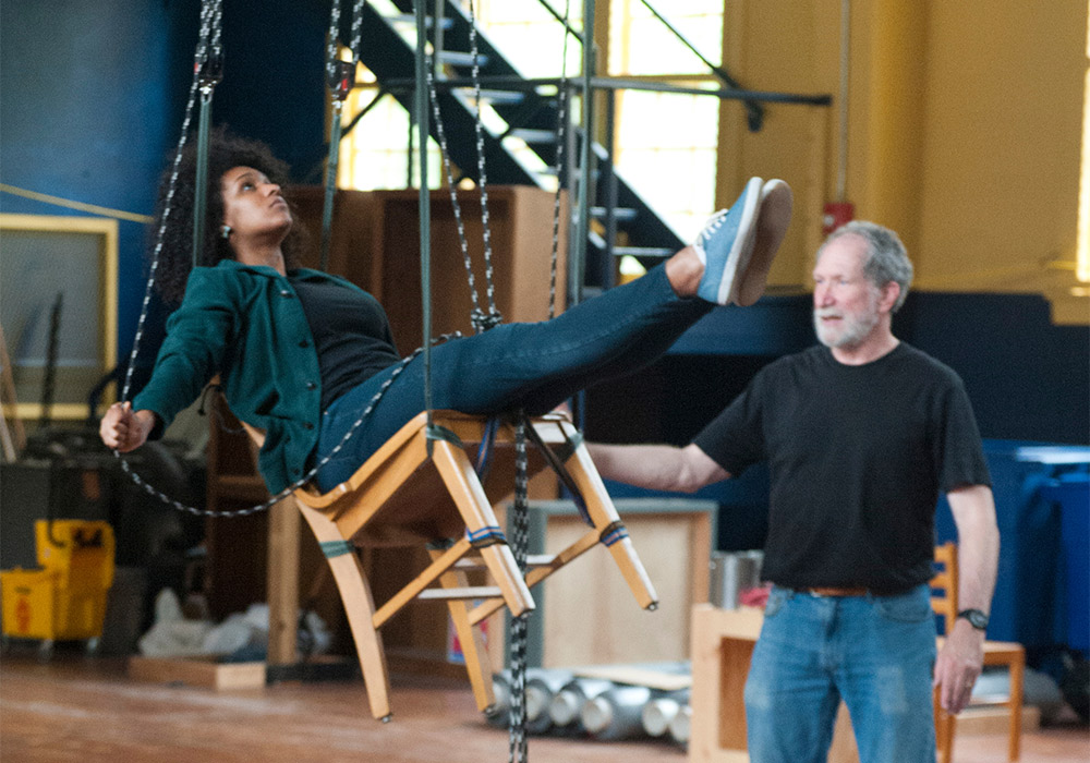 在一场戏剧演出的幕后，一名学生坐在一把用绳子悬挂在空中的椅子上。