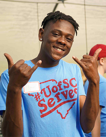 学生穿着UofSC服务t恤，举着马刺手势，对着镜头微笑。