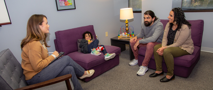 临床医生坐在一个私人房间,一个家族的三个。他们坐在舒适的家具而孩子和大人们说话。