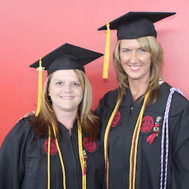 克里斯托·特里布尔和蒂娜·威廉姆森从在线注册护士到BSN课程毕业后，戴着她们的帽子和长袍摆拍。