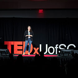Kassy Alia在2018年的活动中站在TEDx的红色标识前。