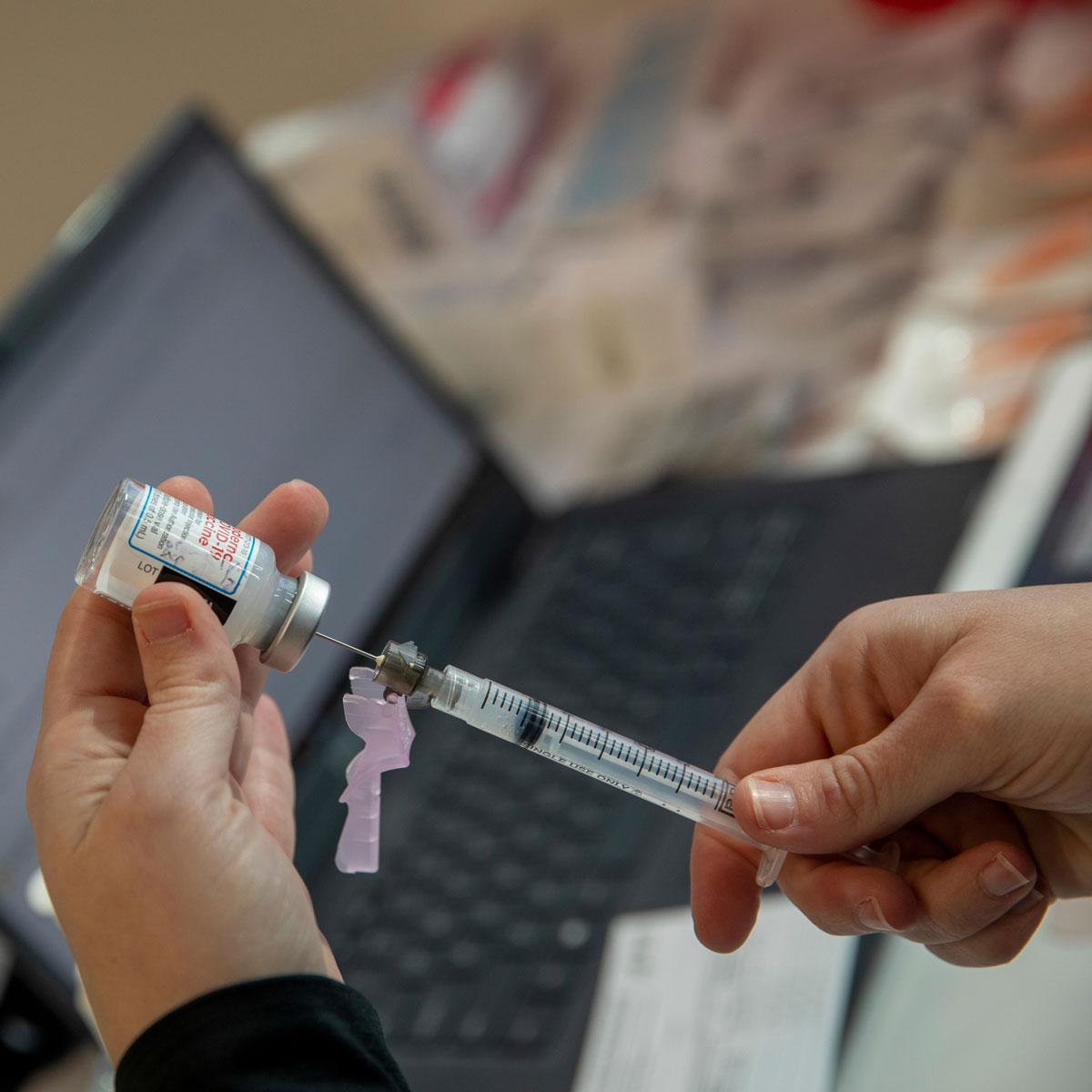 一个医学专业人员用注射器从小瓶中提取疫苗的特写镜头