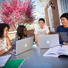 四名学生拿着笔记本电脑坐在SJMC院子里的一张桌子旁